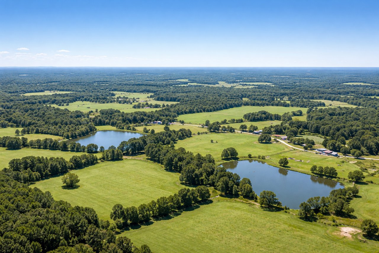 Aerial view of rural fields and woods with two ponds and scattered farm buildings.