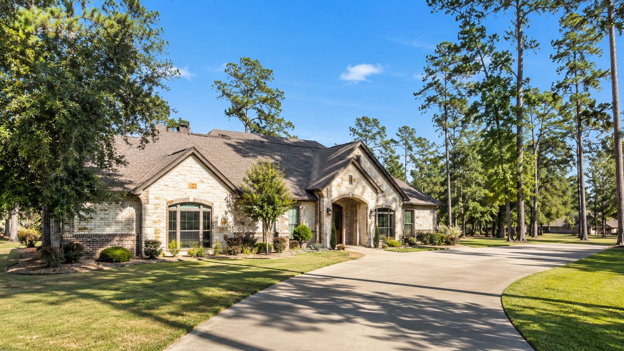 Stone-and-brick home with an arched entry and curved driveway among tall trees.
