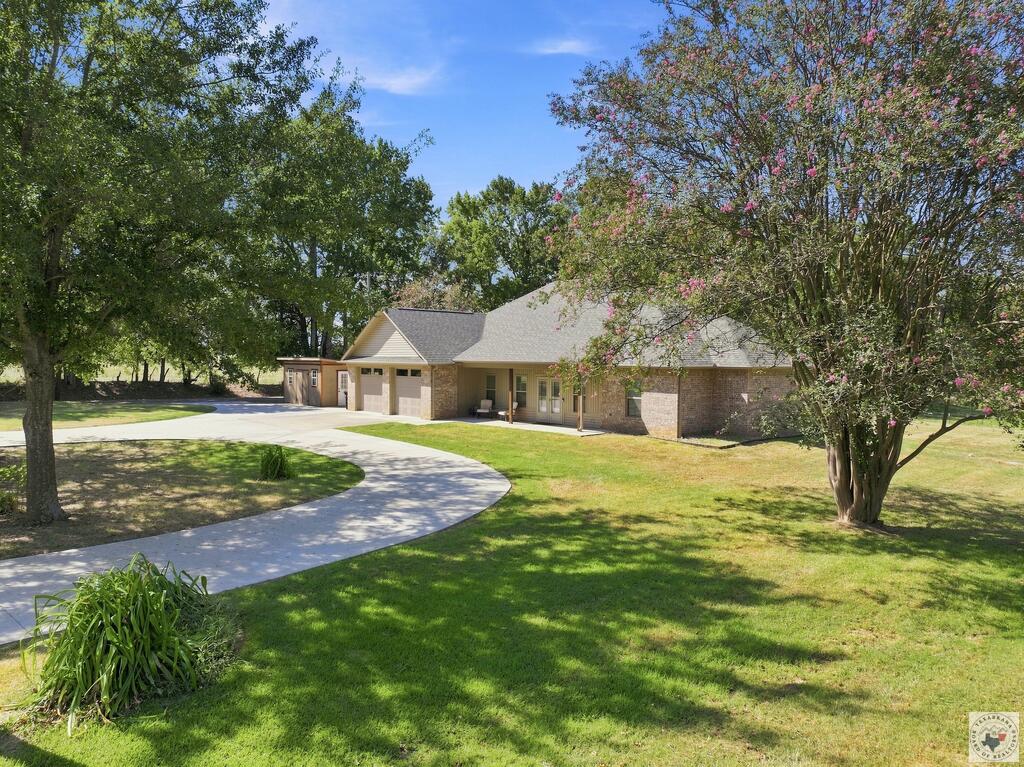Brick home with an attached garage, curved driveway, shaded porch, and flowering crepe myrtle.
