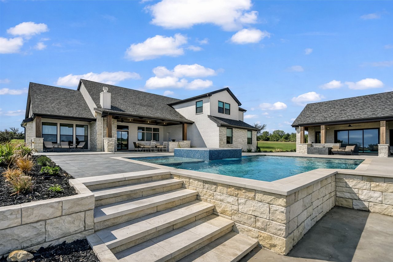 White-and-stone house beside a raised pool, broad patio, and wide stone steps.